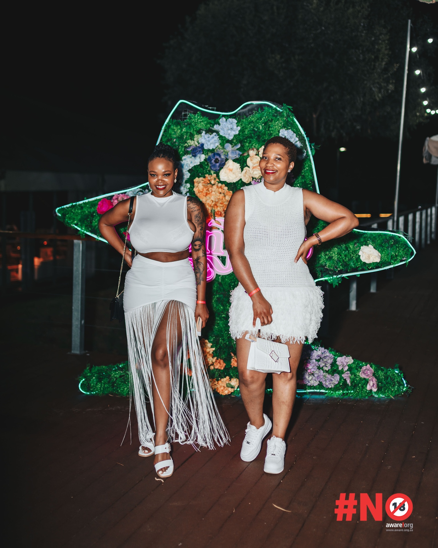 Two guests posing in white outfits by the neon flower backdrop