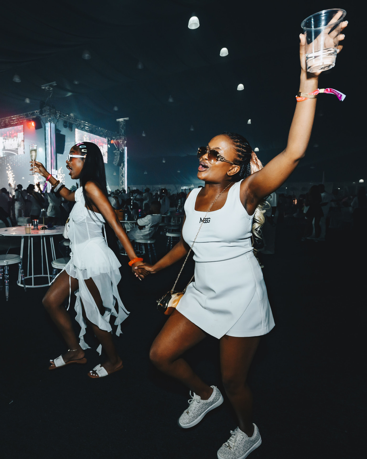 Two guests in white dancing and raising drinks at the party
