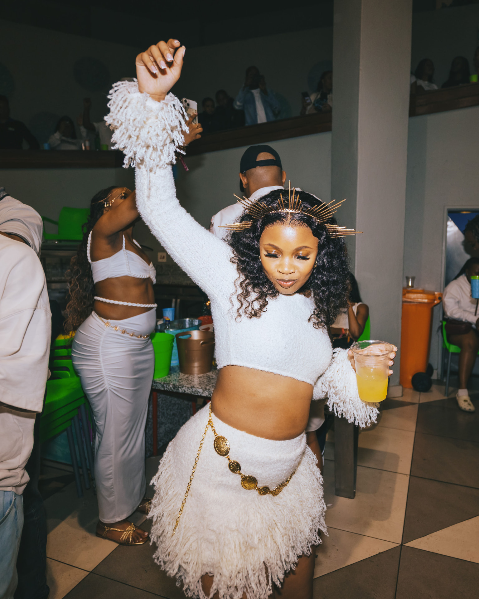 Guest in a white fringe outfit dancing with a drink at the night party